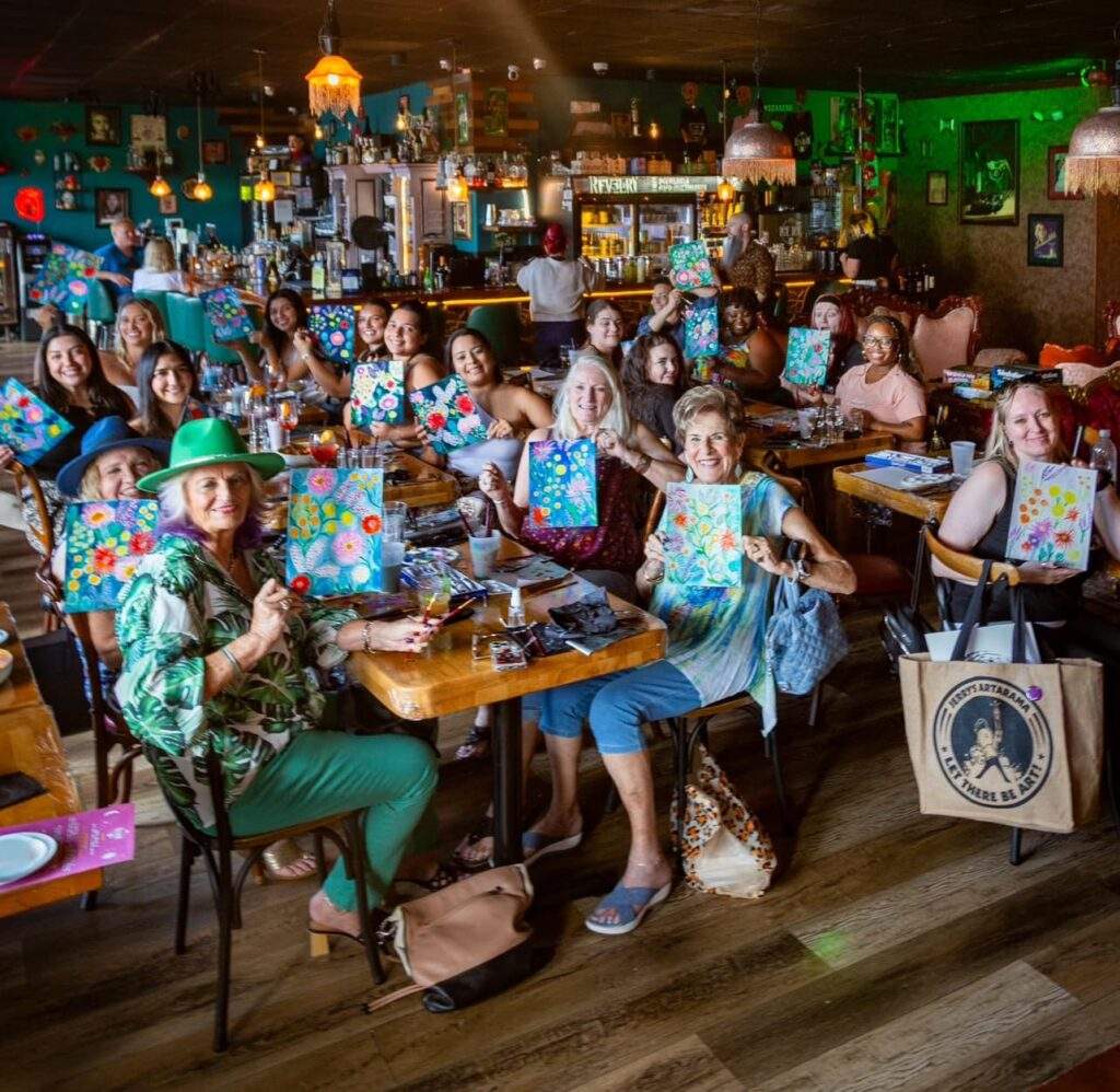 Group of guests celebrating together at Revelry in downtown Pompano Beach during paint and sip event in Pompano Beach, with cocktails, music, and a festive atmosphere.
